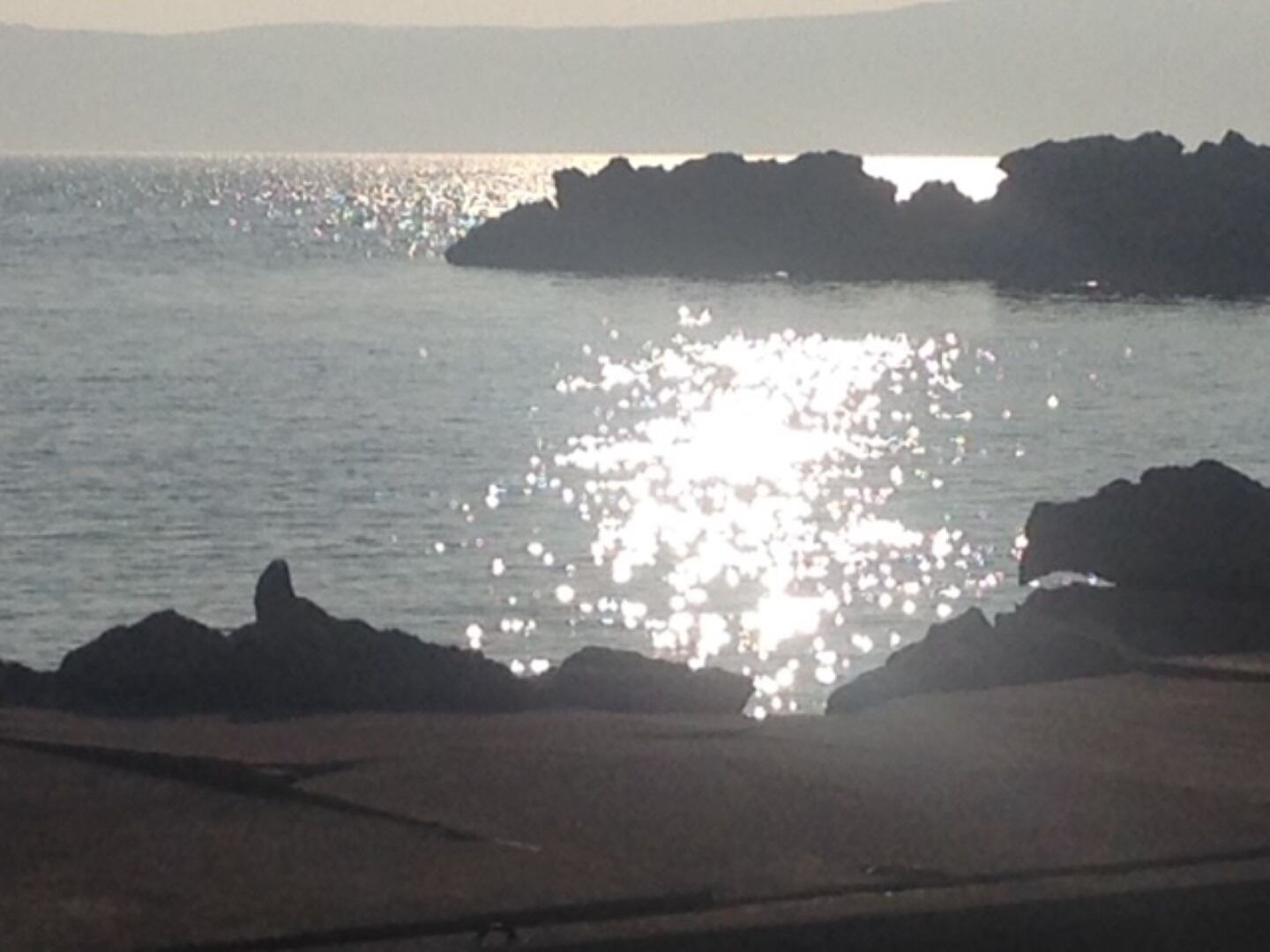 A coastal scene with a rocky shoreline and calm water reflecting sunlight.