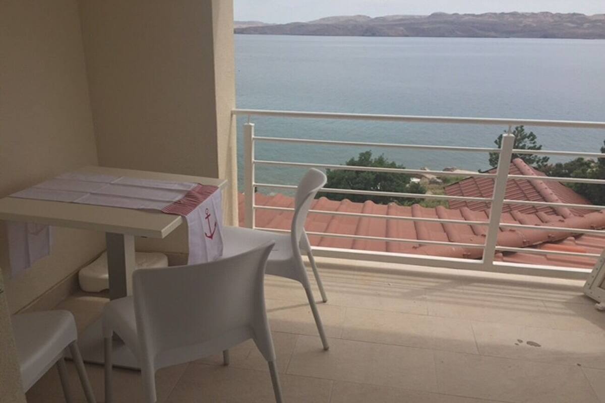 A balcony with a table and chairs, overlooking a body of water and a distant landscape.