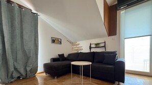 A modern living room with a dark sofa, a small round table, and a wooden floor. - Apartments Neno (Karlobag)