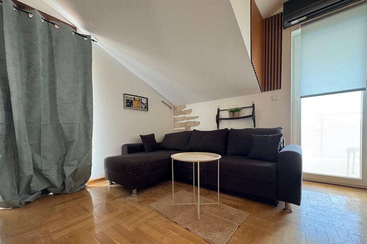 A modern living room with a dark sofa, a small round table, and a wooden floor.