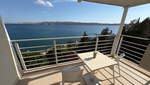 A balcony with a table and chairs, overlooking a body of water and distant land. - Apartments Neno (Karlobag)