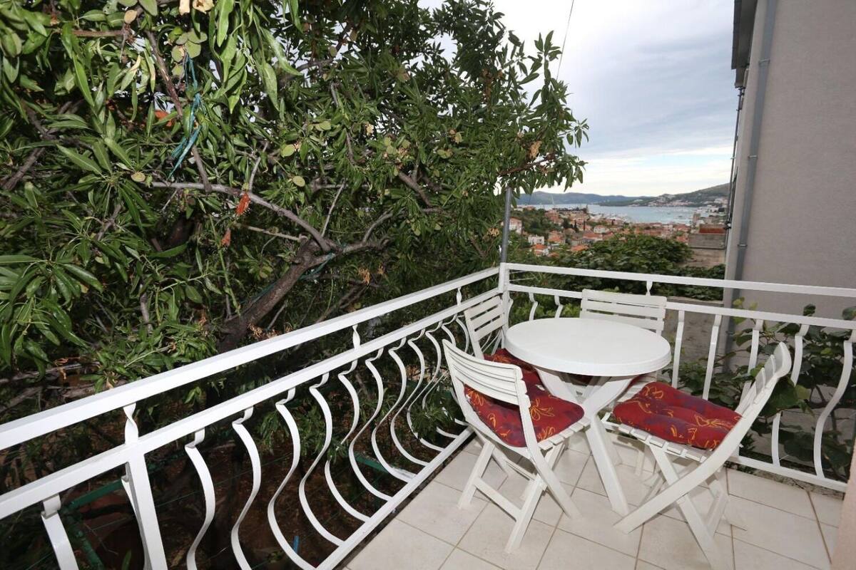 Un balcon doté d’une balustrade en métal blanc, d’une petite table ronde et de deux chaises avec des coussins rouges.