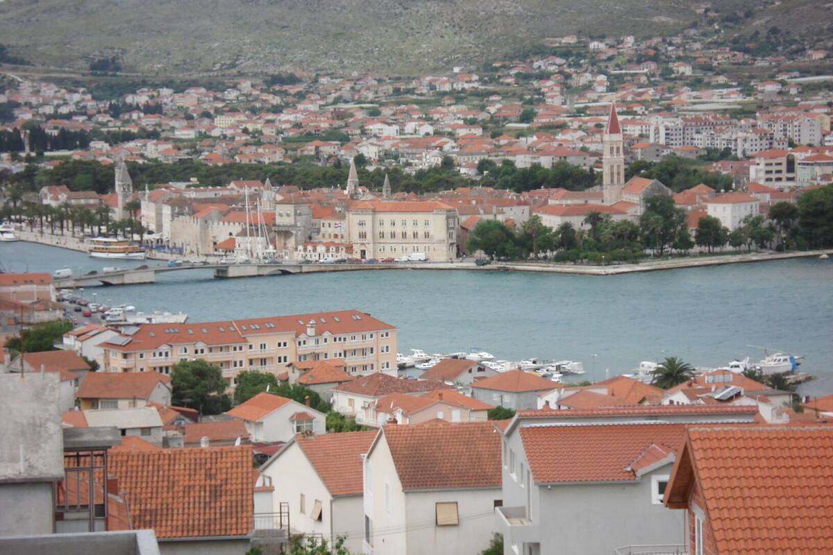 Une ville côtière aux bâtiments aux toits rouges, avec une église imposante et un port de plaisance où sont amarrés des bateaux.