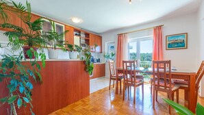 A modern kitchen with wooden cabinets, a dining area with a table and chairs, and a view of the outdoors. - Apartment Mare (Trogir)
