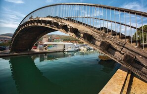 A stone bridge with a metal railing spanning over a body of water, with boats docked below. - Apartment Mare (Trogir)