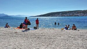 A beach with people sunbathing and swimming, a clear sky, and distant hills. - Apartment Mare (Trogir)