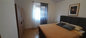 A bedroom with a bed, a nightstand, a door, and a window with curtains. - Apartments Vanja (Vir)