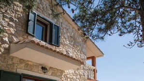 Ένας εξωτερικός χώρος για φαγητό, με ένα πέτρινο κτίριο, πράσινες καρέκλες και ένα τραπέζι στρωμένο για δύο άτομα.