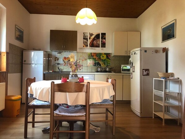 A compact kitchen with white cabinets, a dining table with chairs, a hanging light fixture, and a small refrigerator. - Apartments Durda (Pirovac)