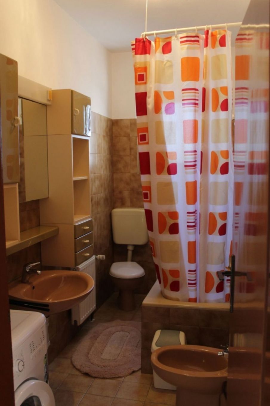 Ein kleines Badezimmer mit Toilette, Waschbecken und Bidet. Eine Duschvorhang mit geometrischem Muster.