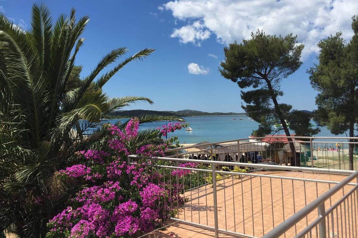 Un balcon avec vue sur la mer, entouré de palmiers et de fleurs violettes.
