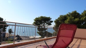 Un balcon avec une chaise rouge, une rambarde en métal et une vue sur la mer.