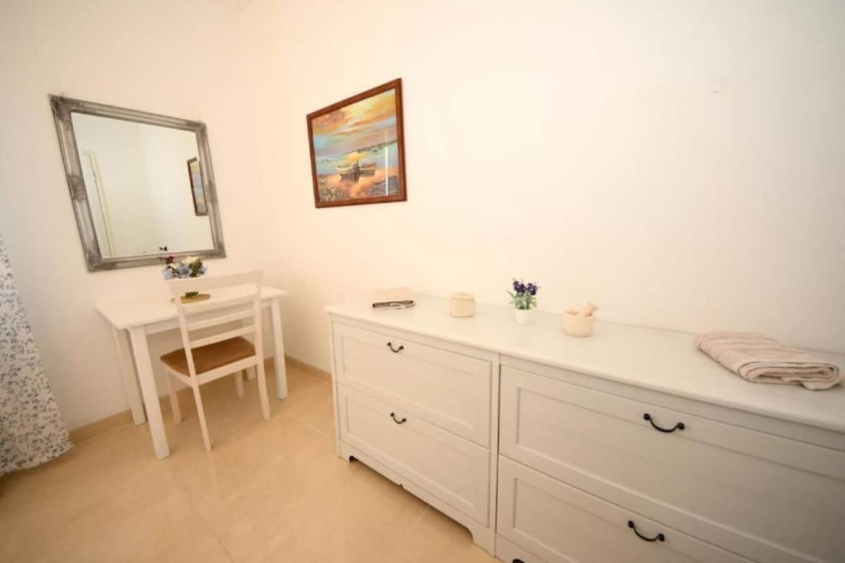 A bathroom with a white vanity, a mirror, a sink, and a cabinet. There is a painting on the wall and a towel on the counter.