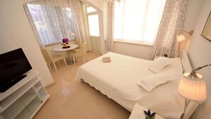 Ein Schlafzimmer mit einem Bett, einem Schreibtisch, einem Stuhl, einem Fernseher und einem Fenster mit Vorhängen.