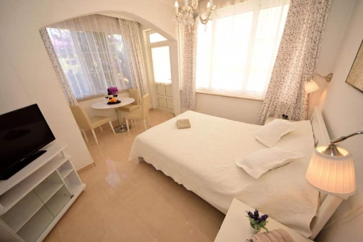 A bedroom with a bed, a desk, a chair, a television, and a window with curtains.