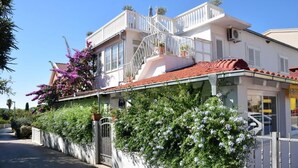 Ein zweistöckiges Gebäude mit Balkon, geschlossenem Eingangsbereich und einem roten Ziegeldach.