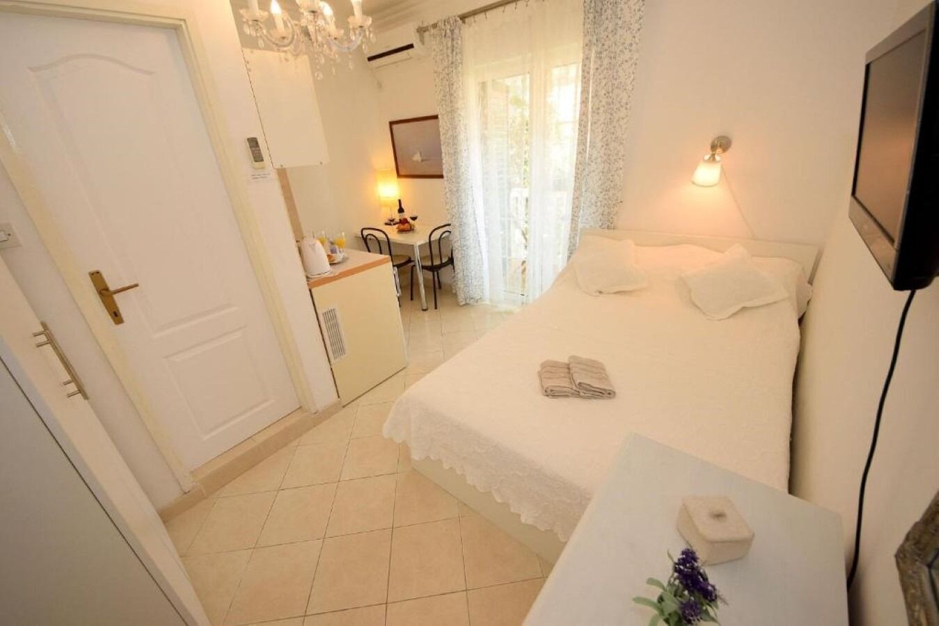 A hotel room with a bed, a desk with a lamp, a small kitchenette, and a bathroom.