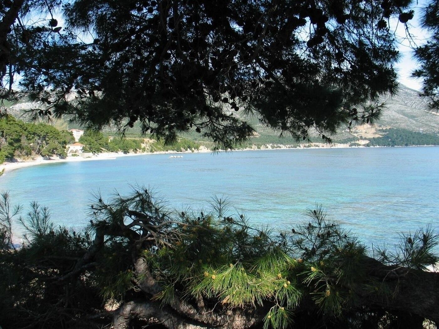 A coastal landscape with a clear blue sea, sandy beach, and a mountainous backdrop.