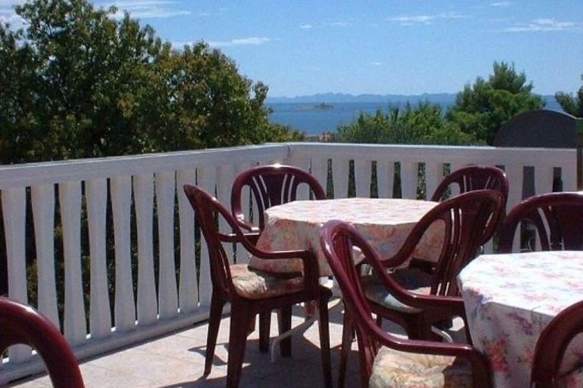 An outdoor patio with round tables and chairs, a white fence, and a view of the sea and mountains in the background.