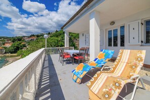 A balcony with a table and chairs, a covered seating area, and a view of the surrounding landscape. - House Ivanka (Karlobag)