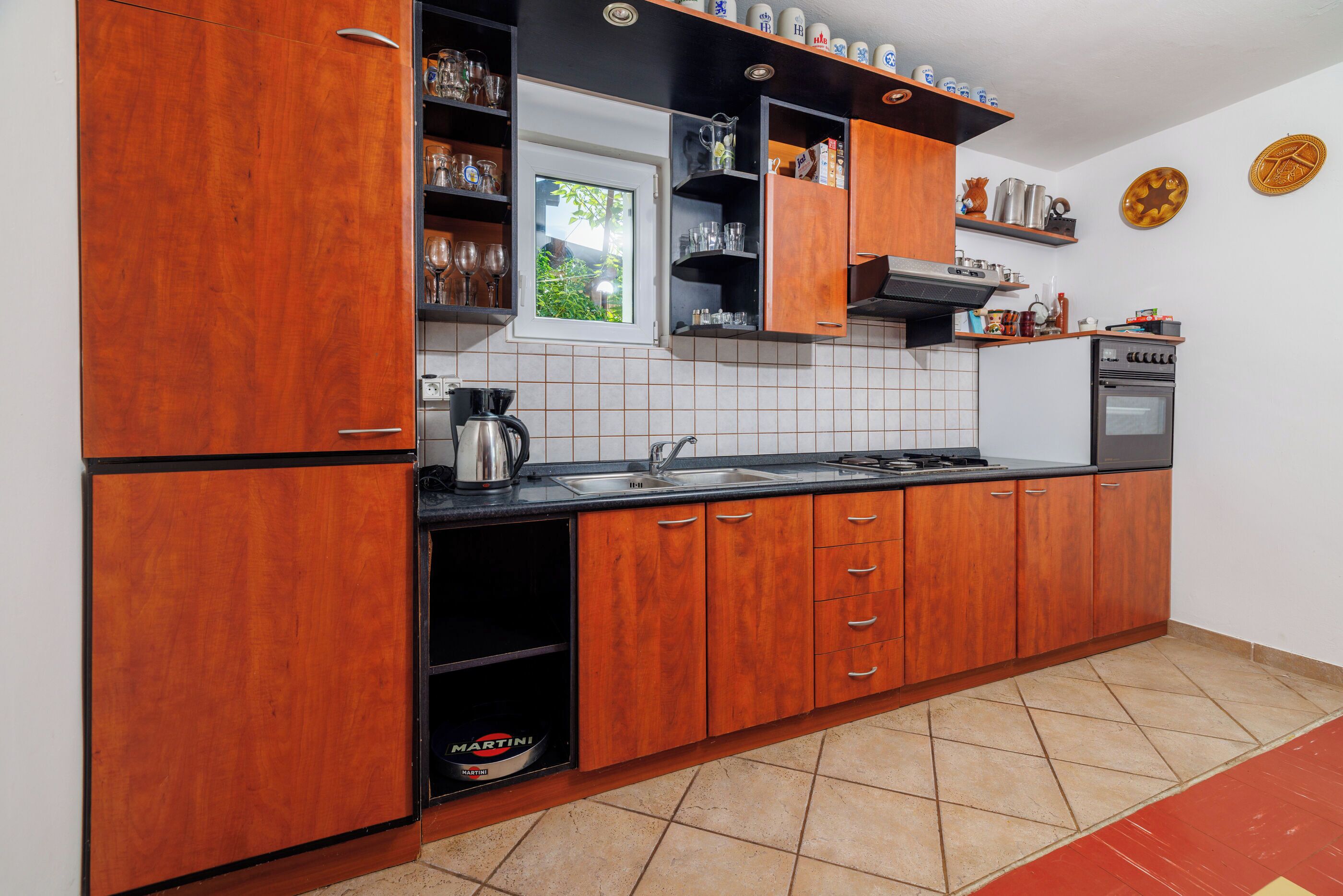 A kitchen with wooden cabinets, a black countertop, a window, and a tiled floor.