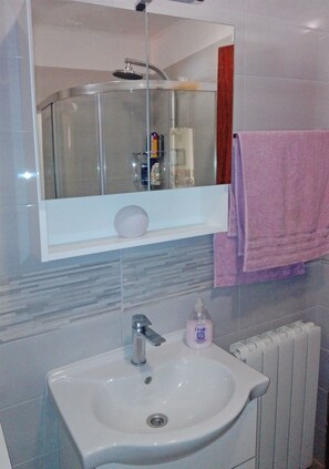 A bathroom with a glass shower enclosure, a white sink with a soap dispenser, and a towel rack with a pink towel. - Apartment Lile (Postira)