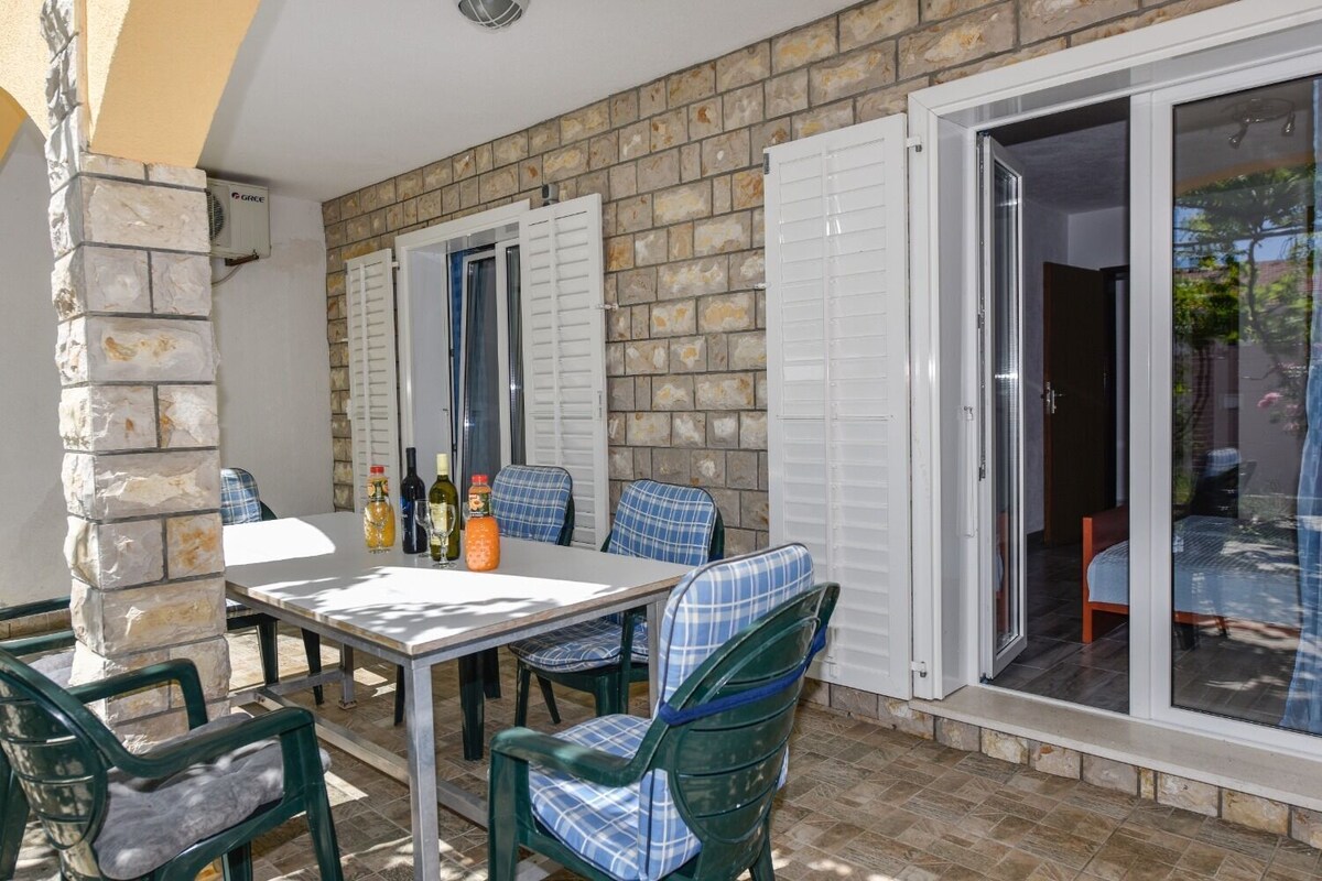 An outdoor patio with a table and chairs, stone walls, and a sliding glass door leading to an interior space.