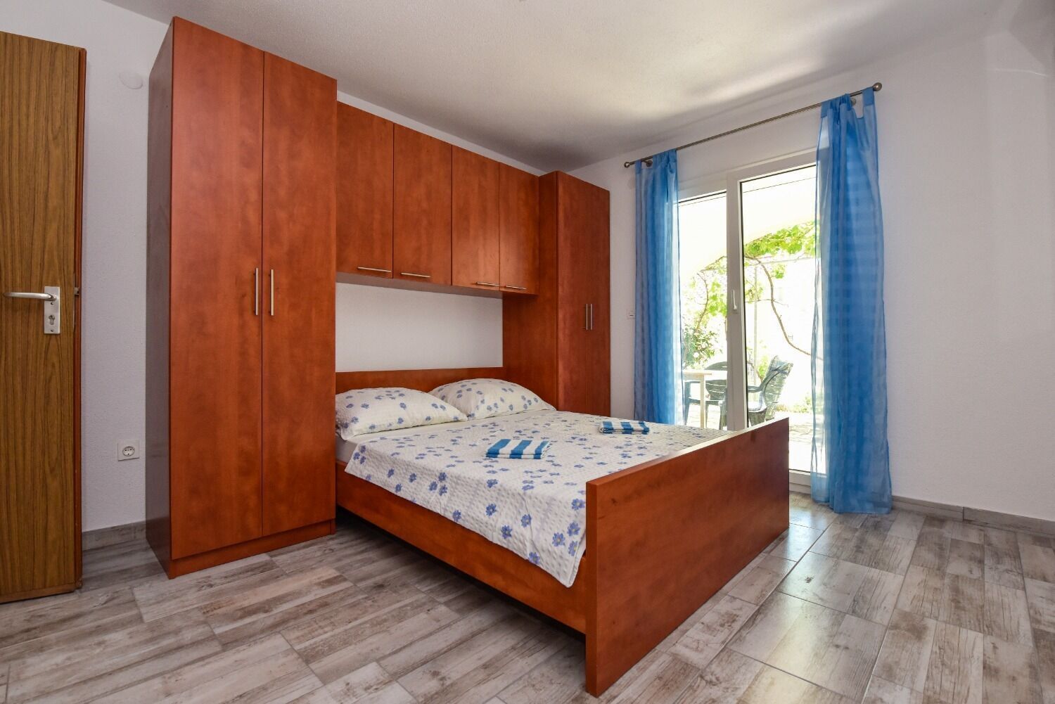 A bedroom with a wooden bed, a wardrobe, and a sliding glass door to a balcony.