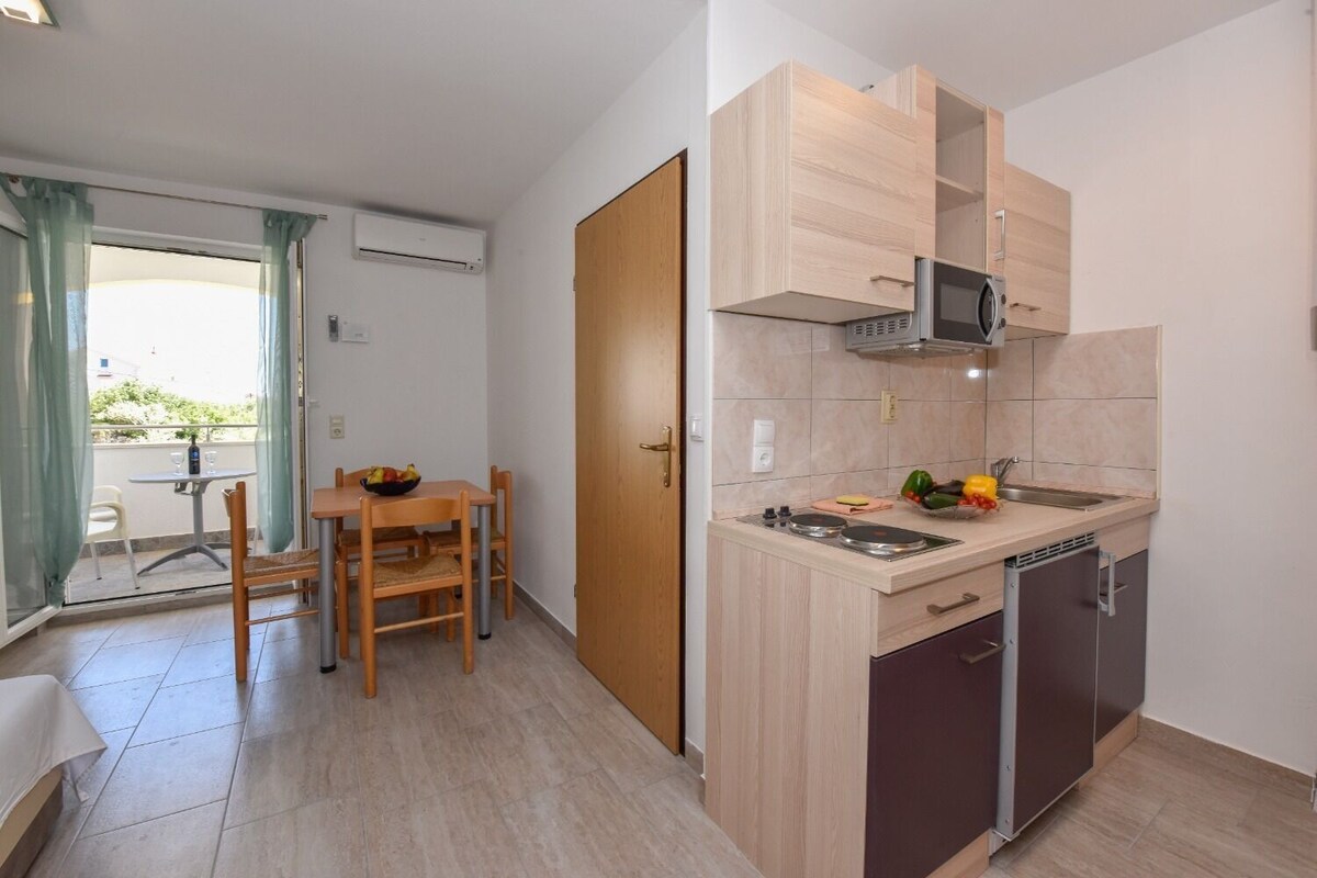 A compact kitchen with a microwave, stove, and dishwasher. There's a dining table with chairs and a small balcony with a table and chairs.