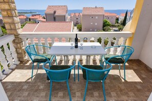 A balcony with a table and four chairs, overlooking a coastal area with red-tiled buildings. - Apartment Mark (Novalja)