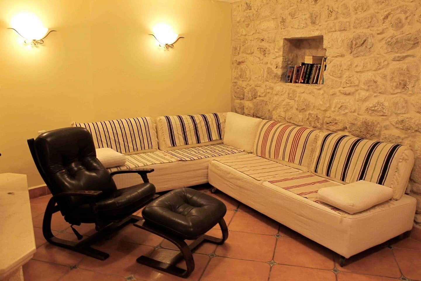 A room with a stone wall, a sofa, a chair, and a small shelf with books.