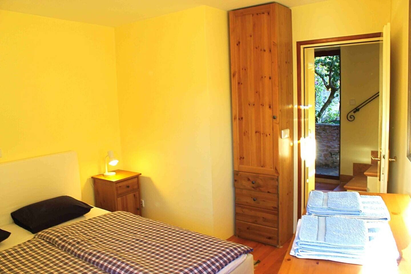 A bedroom with a bed, a nightstand, a wooden wardrobe, and a table with towels.
