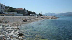 Ein Strand mit klarem Wasser, felsigem Ufer und Gebäuden im Hintergrund.