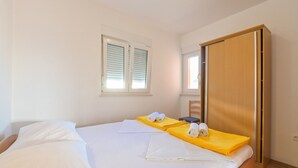 A hotel room with a bed, a wooden wardrobe, a window with blinds, and a chair. - Apartments Ilija (Novalja)