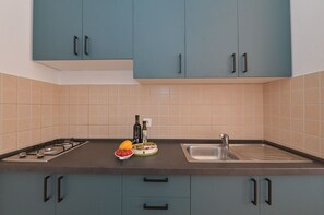 Eine moderne Küche mit türkisfarbenen Schränken, einem Gasherd, einer Spüle und einer Arbeitsfläche mit Obstschale und Olivenölflasche.