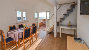 A spacious living area with a dining table, chairs, a staircase, and a balcony with a view. - Apartments Ilija (Novalja)