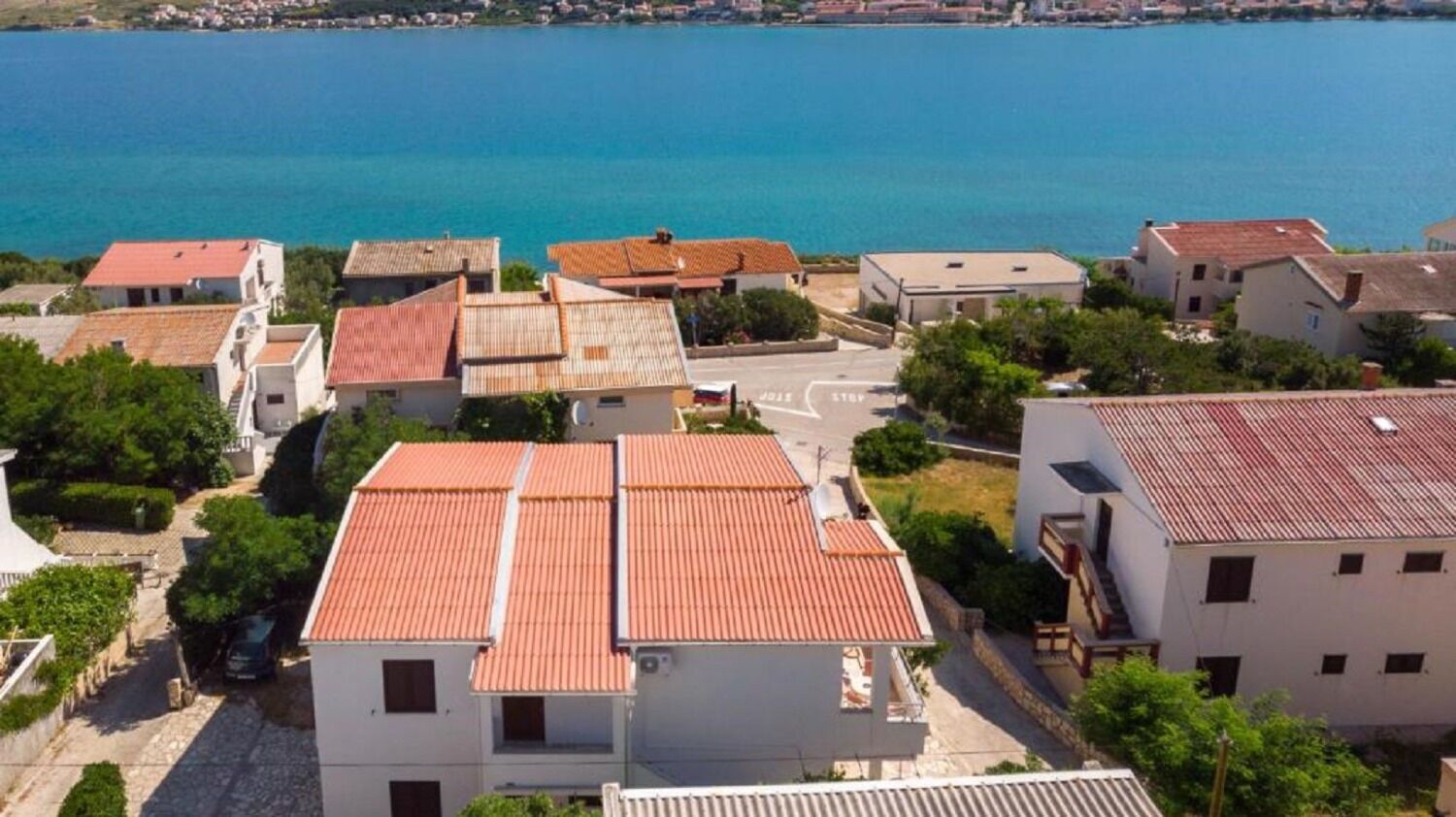 Ein Küstenwohngebiet mit Häusern mit Terrakotta-Dächern, blauem Meer und einer asphaltierten Straße.