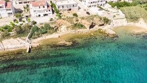 An aerial view of a coastal area with clear turquoise waters, buildings, and greenery. - Apartments Marko (Pag)