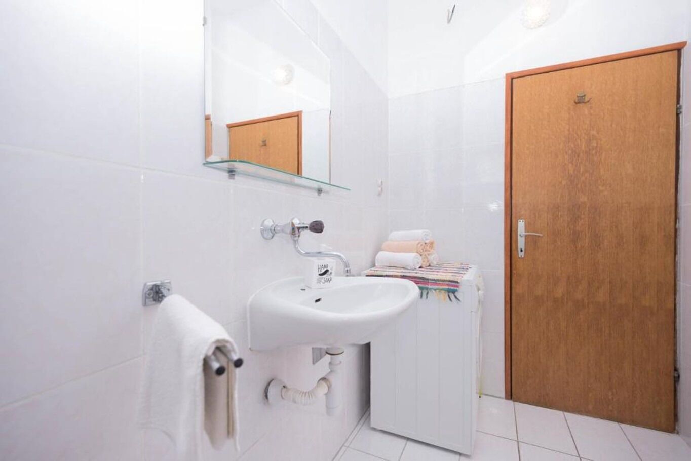 Un baño con un lavamanos blanco, un espejo, un perchero para toallas y una puerta de madera.