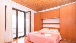 A bedroom with a wooden ceiling, a bed with pink bedding, and a sliding glass door leading to an outdoor area. - Apartments Marko (Pag)