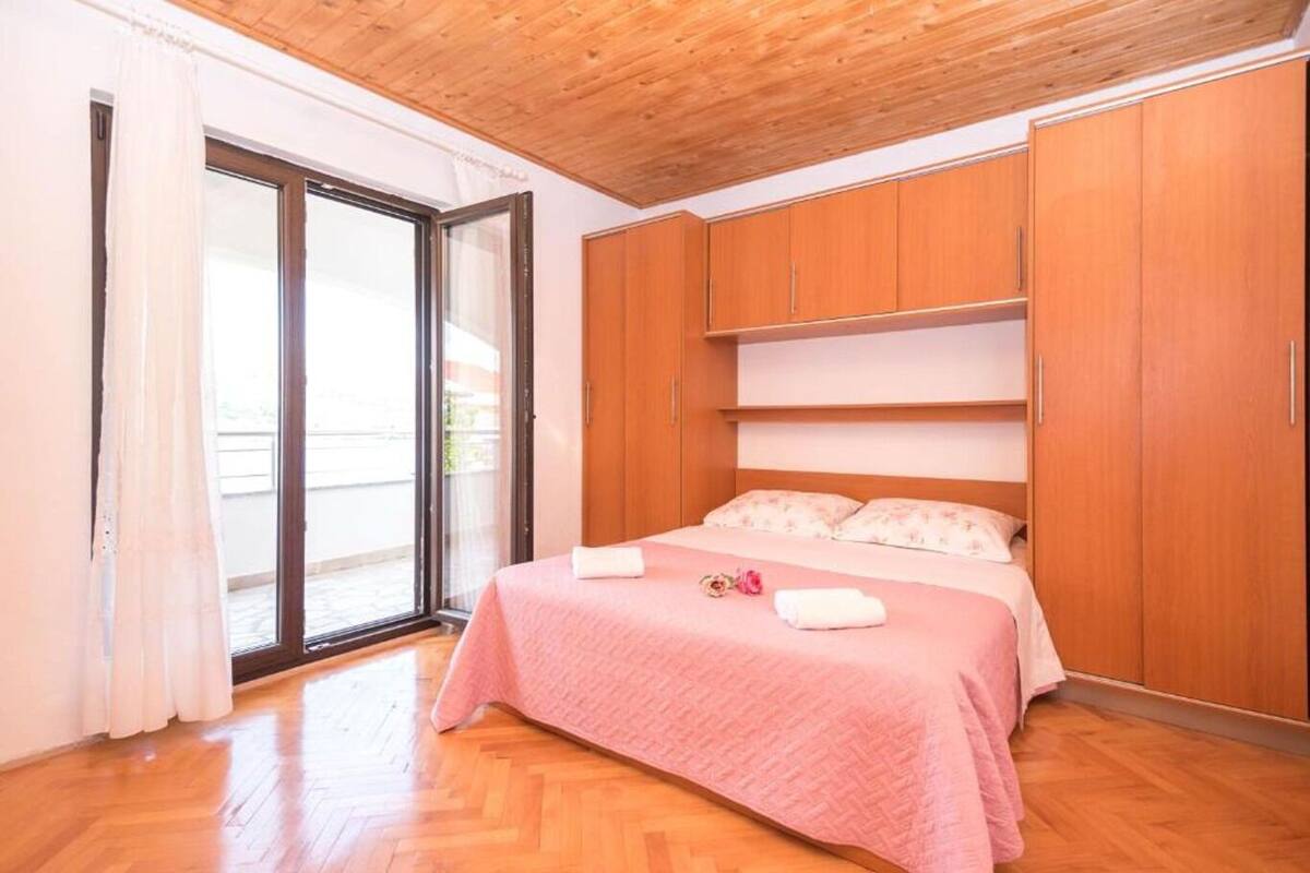 A bedroom with a wooden ceiling, a bed with pink bedding, and a sliding glass door leading to an outdoor area.