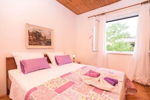A bedroom with a bed, pillows, a painting, a window, and curtains. - Apartments Marko (Pag)