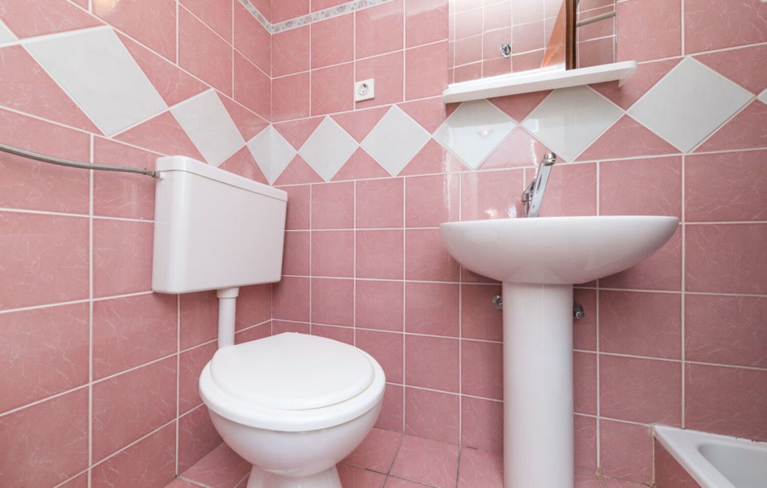 A bathroom with pink tiles, a white toilet, and a white sink.