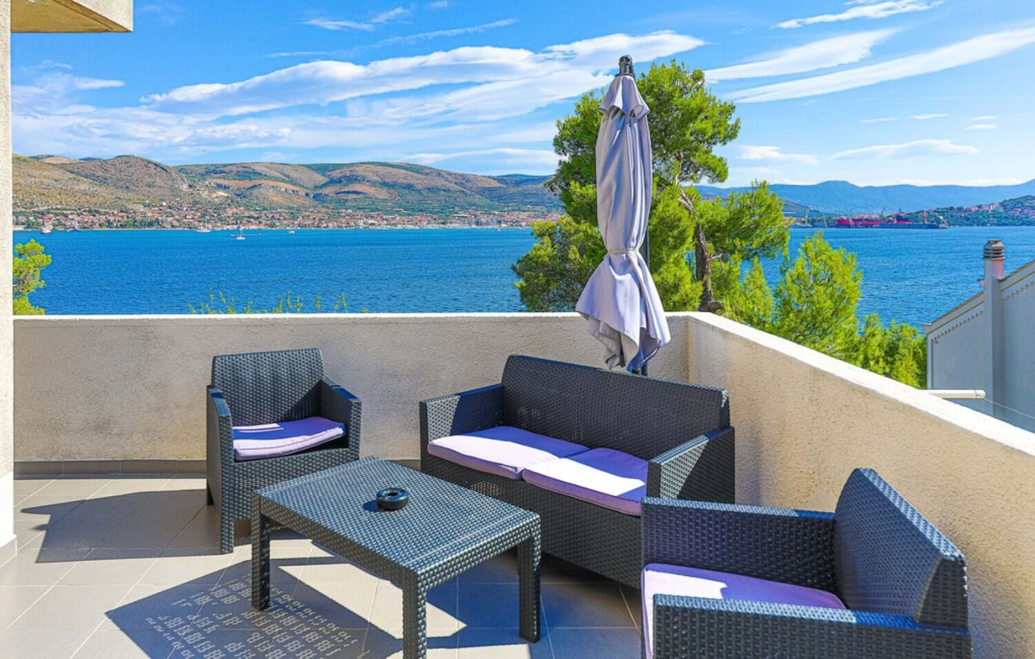 A balcony with wicker furniture, a table, and an umbrella.