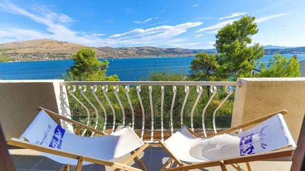 Un balcón con dos sillones blancos frente a una vista panorámica de un lago y montañas.
