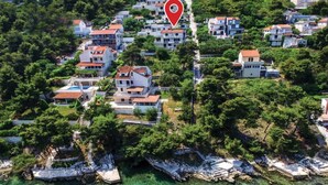Vista aérea de una zona residencial costera con casas, un marcador rojo de ubicación y aguas turquesas cristalinas.