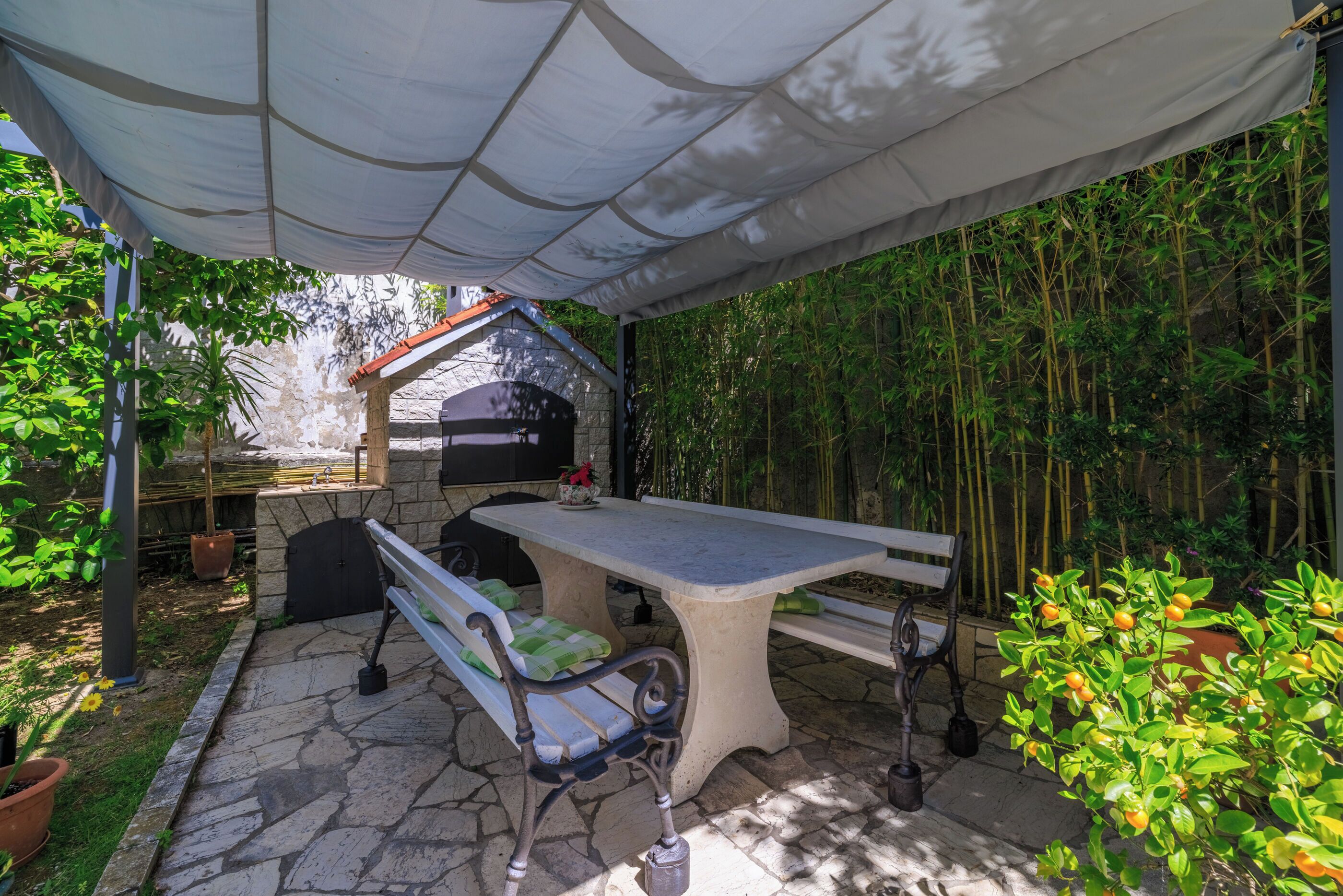 An outdoor patio with a stone table and benches, surrounded by bamboo plants and potted plants.