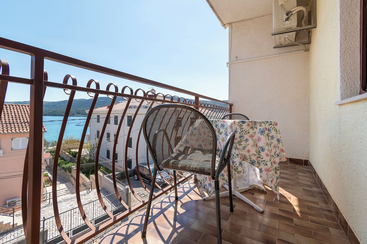A balcony with a metal railing, a chair, and a table with a floral tablecloth.
