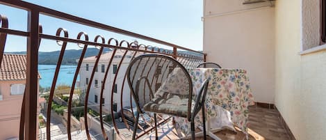 Un balcon avec une balustrade en métal, une chaise et une table recouverte d’une nappe à motifs floraux.