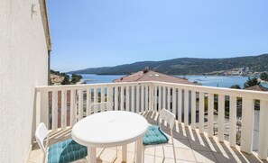 A balcony with a white table and chairs, overlooking a coastal view with a clear sky. - Apartments Pera (Marina)